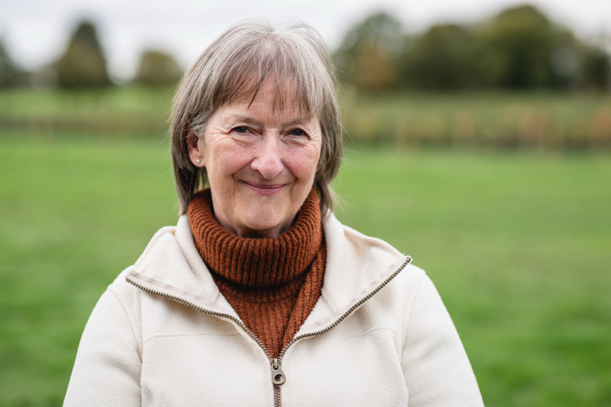 Portrait of a senior woman standing in a field while at a farm in Autumn, smiling while looking at the camera.