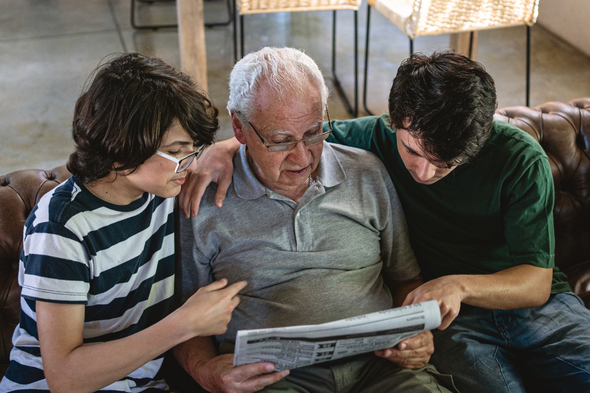 Young boys reading newspaper with their senior adult grandfather in the living room